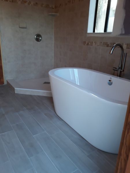 Modern bathroom with white tub, walk-in shower, and wood-look tile floors.