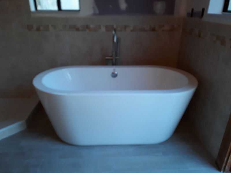 Freestanding white bathtub in a bathroom with beige walls and a silver faucet.