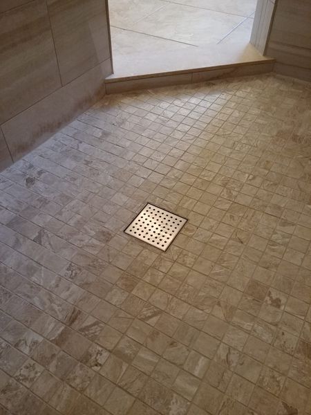 Bathroom floor with small beige tiles, shower drain in the center. Light beige walls.