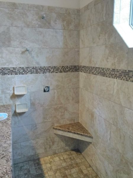 Tiled shower with corner seat and decorative band. Light beige and brown tones.