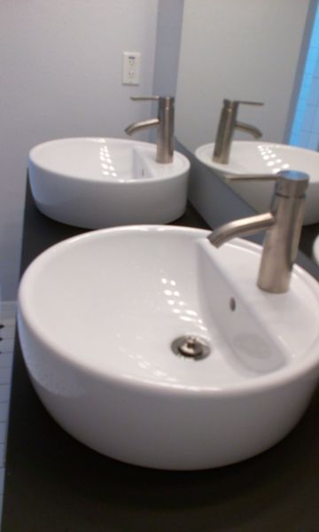 Three white ceramic bowl sinks with brushed nickel faucets on a black countertop, reflected in a mirror.