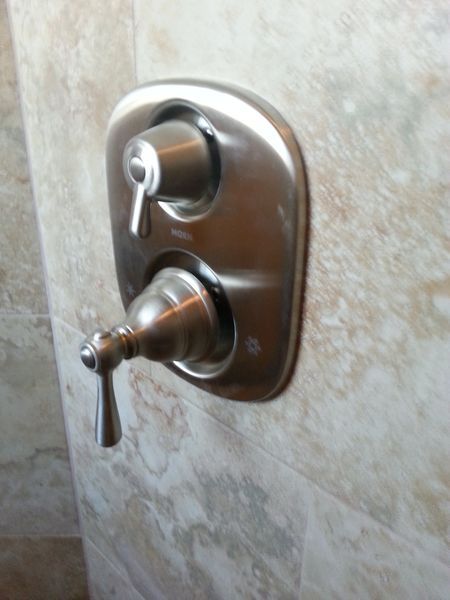 Shower faucet controls with two levers on tiled wall.