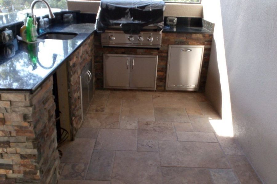 Outdoor kitchen with stone accents, granite countertops, built-in grill, and tiled floor.