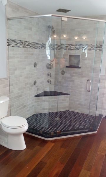 Modern bathroom with glass shower enclosure, dark tiled floor, and light tile walls. Toilet and hardwood floor.