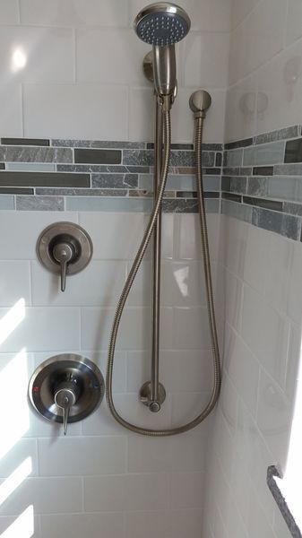 Shower with brushed nickel fixtures and white and blue tiled walls.