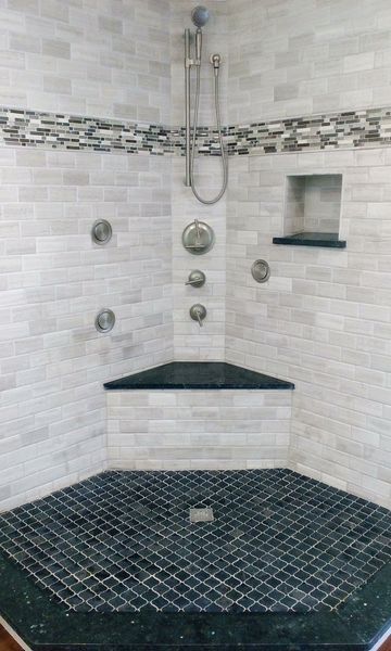 Corner shower with black and white tile, showerheads, built-in shelf, and a triangle-shaped seat.