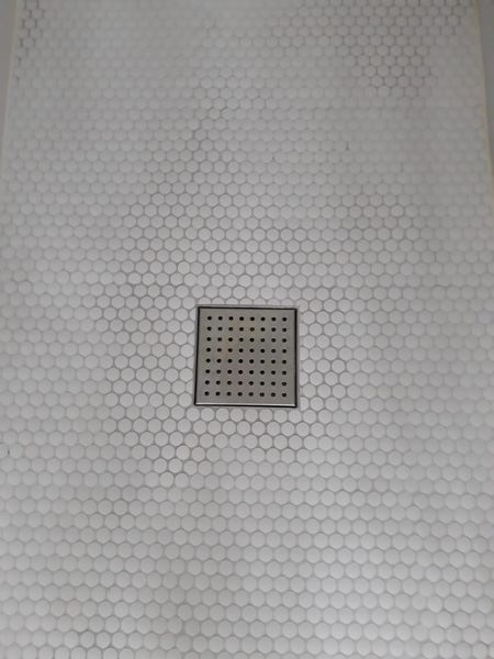 White hexagon tile shower floor with a square drain.