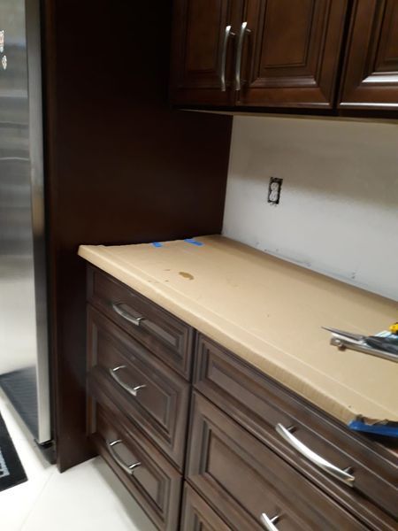 Kitchen counter and cabinets. Dark wood cabinets with tan countertop. Wall outlet and stainless steel refrigerator.