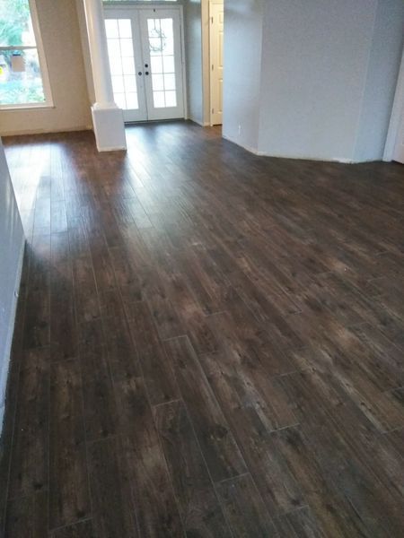 Dark brown wooden-look flooring in a room with white walls and a double door in the background.