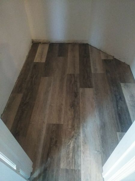 Brown and gray wood-look floor installed in an angled alcove, bordered by white walls and trim.