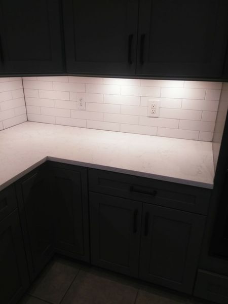 Kitchen corner with white countertop, subway tile backsplash, gray cabinets, and under-cabinet lighting.