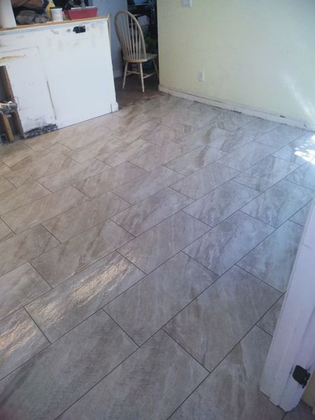 Tiled floor in a kitchen with a white cabinet, chair, and light-colored walls.