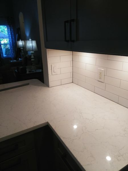 Kitchen countertop with white subway tile backsplash, under-cabinet lighting, and dark blue cabinets.
