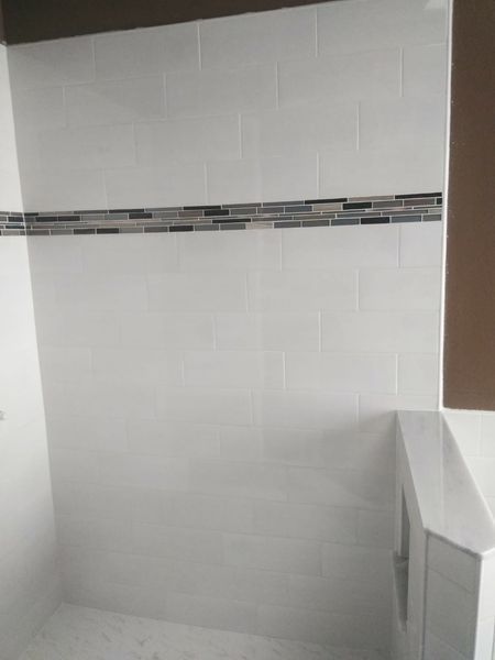 White tiled shower with a decorative mosaic tile stripe, brown trim.