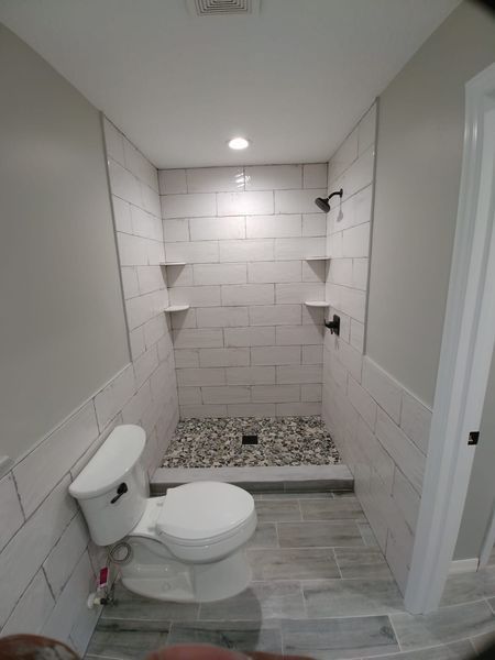 Modern bathroom with a tiled shower, stone floor, and a toilet.