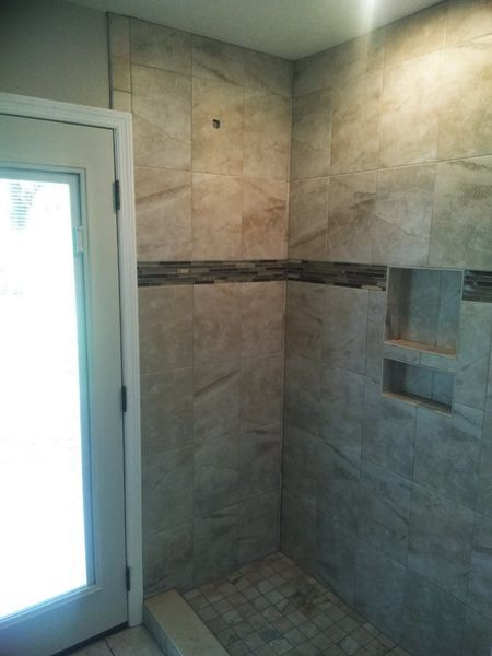 Tiled shower with a niche and accent band. Door frame on left. Light shining through the door.