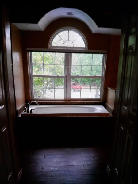Bathroom with a built-in tub under a window. Dark wood, tiled floor, natural light.