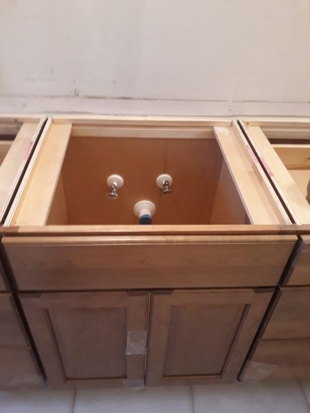 Wooden bathroom vanity cabinets with space for a sink and exposed plumbing.