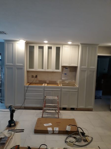 Kitchen cabinets being installed, with a step ladder, drill, and tools present.