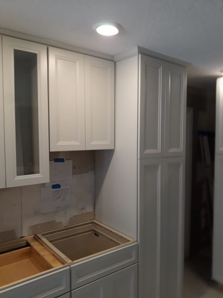 White kitchen cabinets under construction; upper cabinets installed, lower cabinets ready for drawers.