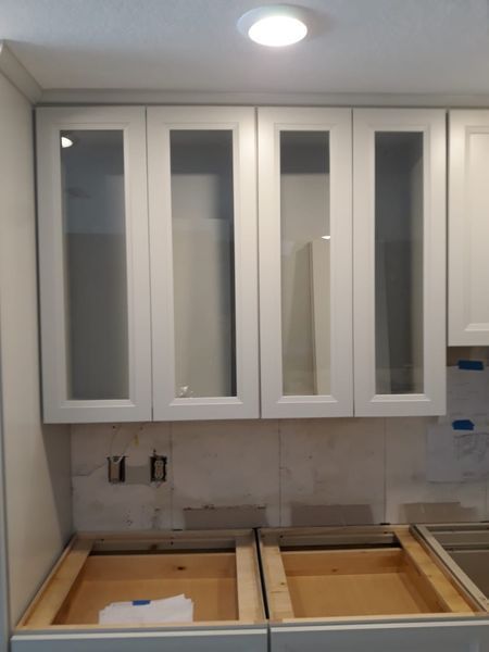 White kitchen cabinets with glass inserts above unfinished lower cabinets.