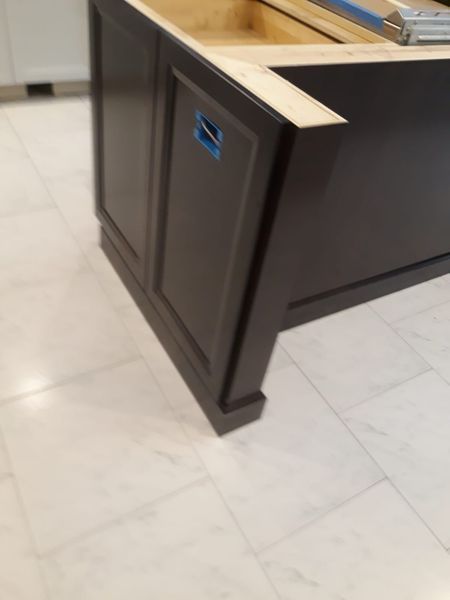 Dark gray kitchen island cabinet with decorative paneling, built on a marble tile floor.