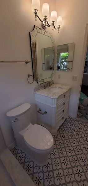 Bathroom with patterned floor, white vanity with mirror and sink, toilet, and chandelier lighting.