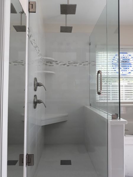Modern white tiled shower with glass doors, two shower heads, and built-in bench.