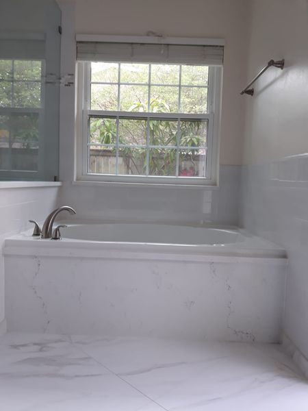White tiled bathroom with a bathtub under a window.