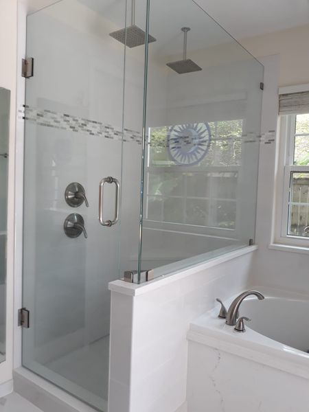 Glass shower with two showerheads, a tub, and white tile.