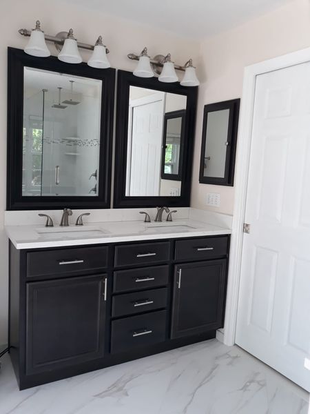 Bathroom with dark vanity, white countertop, matching mirrors, and bright lighting.