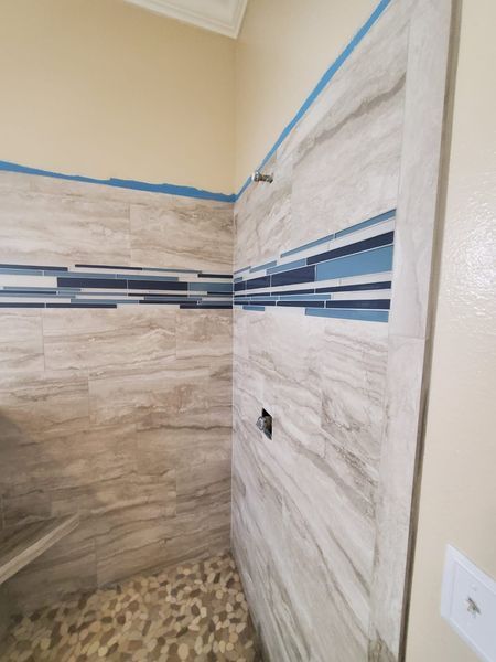 Shower with stone tile walls, a blue tile accent, and pebble floor.