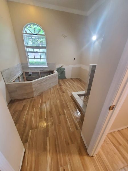 Bathroom renovation: light wood-look floor, tub surround, unfinished walls, arched window, entry door.