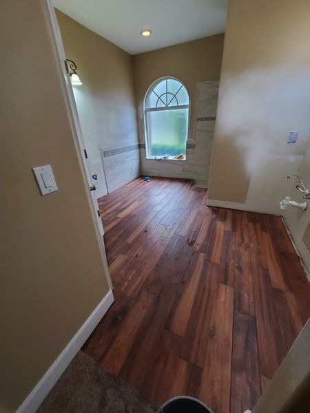 Bathroom with dark wood floors, arched window, and unfinished walls with neutral paint.