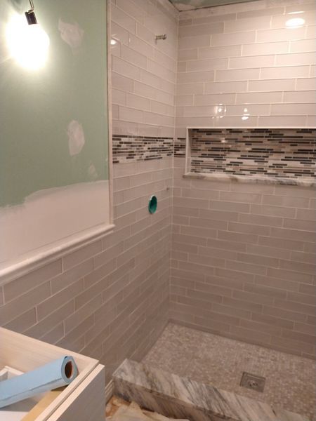 Tiled shower with a niche and pebble floor, under construction, light gray and accent tile.