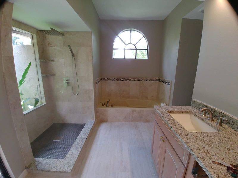 Bathroom with shower and tub; beige tile, light wood floors, granite countertop, arched window.