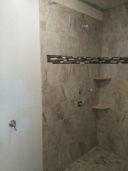 Tiled shower with beige walls, a decorative tile border, two shelves, and a showerhead.