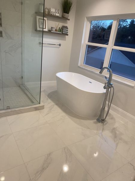 Modern bathroom with white freestanding tub, glass shower, and large window.