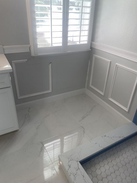 Bathroom corner with white marble floor, gray walls, white trim, and a window with shutters.