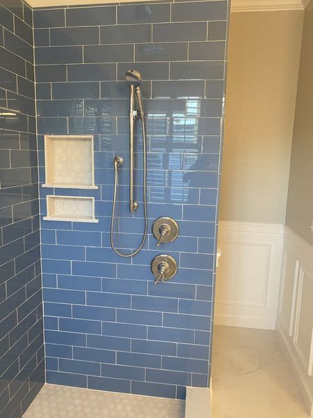 Blue tiled shower with silver fixtures and built-in shelving next to a light-colored wall.