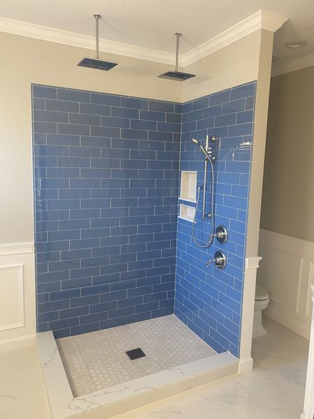 Blue tiled shower with two rain shower heads, a handheld shower, and a white tiled floor.