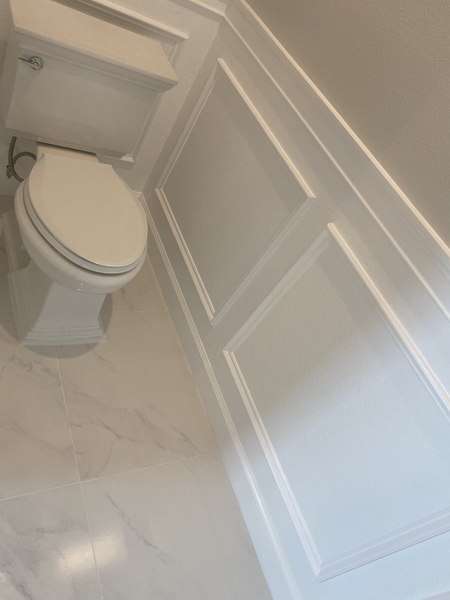 White toilet and wainscoting in a bright, modern bathroom with marble-look floor tile.