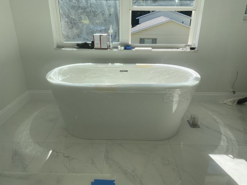 White freestanding bathtub in a bathroom with marble flooring and a window.