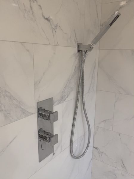 Shower with stainless steel fixtures against white marble-like tile.