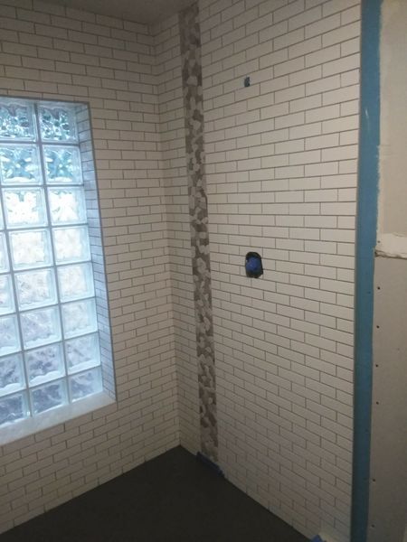 White brick-style tiled shower with glass block window, gray floor, and patterned accent strip.