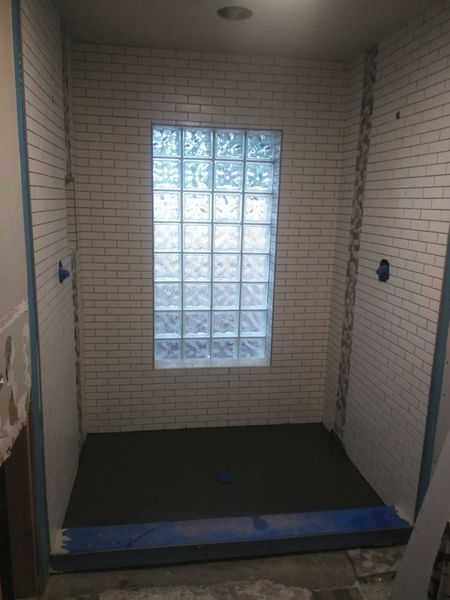 Shower stall with white brick tile, glass block window, dark floor.