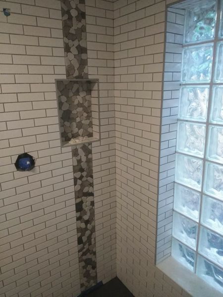 Tiled shower with a niche and glass block window. White subway tile, stone accent, and blue fixture.