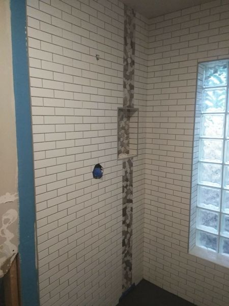 Shower walls tiled with white subway tile, a strip of decorative tile and a glass block window.