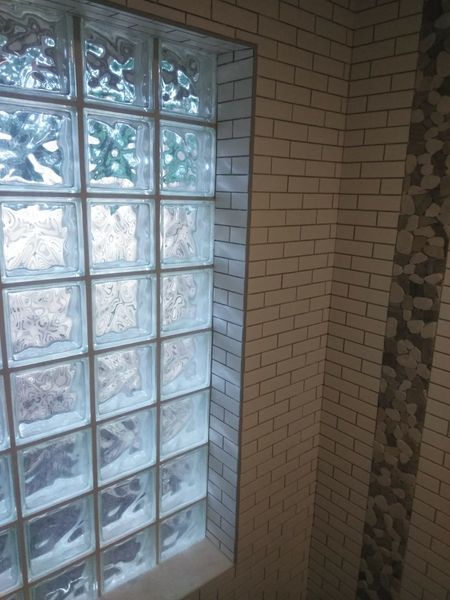 Glass block window in a tiled bathroom, with white brick-like tiles and a stone accent.