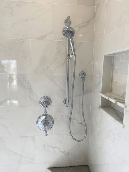 Shower with marble-look tile, chrome fixtures, a hand shower, and a recessed shelf.